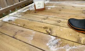 En flaska linoljesåpa står på en altan som håller på att rengöras. En svart stövel med orange kant syns i nedre högra hörnet.