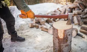 Person i handskar förbereder sig för att hugga ved. En yxa vilar på en trädstam, omgiven av snö och huggen ved.