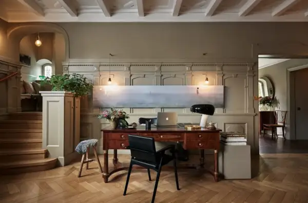 Ett elegant skrivbord med laptop och lampa, i en hall med trappa och konst. Martin Brudnizki-inspirerad design.